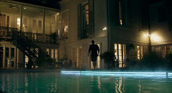 Movie still from “Deep Water” (2022), directed by Adrian Lyne – A man standing next to a swimming pool at night; Extreme Wide shot, Low angle