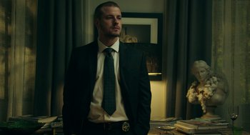 Movie still from “Deep Water” (2022), directed by Adrian Lyne – A man in a suit and tie standing in a room; Medium shot, Low angle