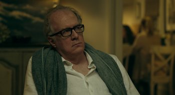 Movie still from “Deep Water” (2022), directed by Adrian Lyne – An older man wearing glasses and a white shirt; Close Up shot, Over the shoulder angle