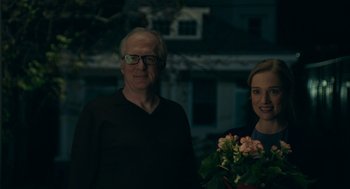 Movie still from “Deep Water” (2022), directed by Adrian Lyne – An older man standing next to a young woman holding flowers; Close Up shot, Over the shoulder angle