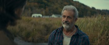 An older man in a plaid shirt is standing in a field