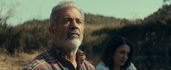 An old man with a beard and a woman in the background