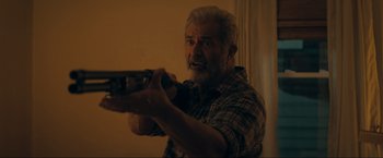 An older man holding a gun in a room