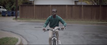 Movie still from “Upstream Color” (2013), directed by Shane Carruth – A man riding a bicycle down a street; Wide shot, Over the shoulder angle
