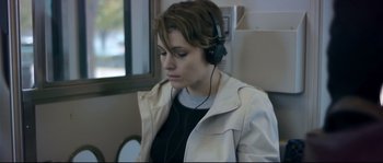 Movie still from “Upstream Color” (2013), directed by Shane Carruth – A woman wearing headphones and sitting in front of a window; Close Up shot, Over the shoulder angle