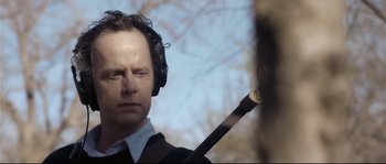 Movie still from “Upstream Color” (2013), directed by Shane Carruth – A man in a suit and headphones holding a sword; Close Up shot, Over the shoulder angle