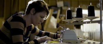 Movie still from “Upstream Color” (2013), directed by Shane Carruth – A woman working on a sewing machine in a room; Medium shot, Low angle