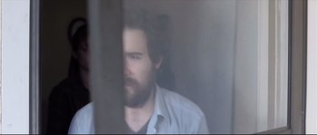 Movie still from “Upstream Color” (2013), directed by Shane Carruth – A man with a beard is looking out of a window; Close Up shot, Over the shoulder angle