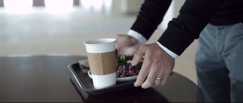 Movie still from “Upstream Color” (2013), directed by Shane Carruth – A person holding a cup of coffee over a tray of food; Extreme Close Up shot, Over the shoulder angle