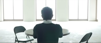 Movie still from “Upstream Color” (2013), directed by Shane Carruth – A man sitting at a table in front of a large window; Medium shot, Low angle