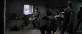 Movie still from “Die Another Day” (2002), directed by Lee Tamahori – A man in a military uniform sitting in front of another man; Wide shot, Over the shoulder angle