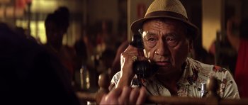 Movie still from “Die Another Day” (2002), directed by Lee Tamahori – An older man talking on a phone while sitting at a table; Close Up shot, Low angle