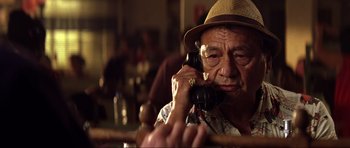 Movie still from “Die Another Day” (2002), directed by Lee Tamahori – An older man talking on a phone while sitting at a table; Close Up shot, Low angle