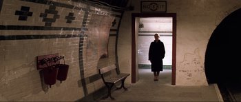 Movie still from “Die Another Day” (2002), directed by Lee Tamahori – An older woman standing in front of an exit sign; Wide shot, High angle