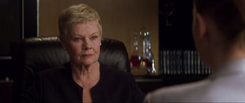 Movie still from “Die Another Day” (2002), directed by Lee Tamahori – An older woman sitting in a chair in a room; Close Up shot, Over the shoulder angle