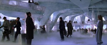 Movie still from “Die Another Day” (2002), directed by Lee Tamahori – A group of people standing around in a room; Extreme Wide shot, High angle