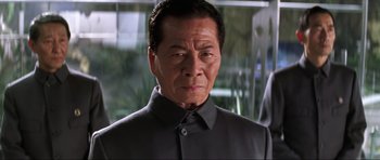 Movie still from “Die Another Day” (2002), directed by Lee Tamahori – An older man wearing a black shirt and a black jacket; Close Up shot, Low angle