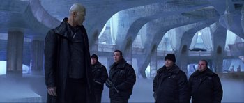 Movie still from “Die Another Day” (2002), directed by Lee Tamahori – A group of men standing next to each other in a room; Medium shot, Low angle