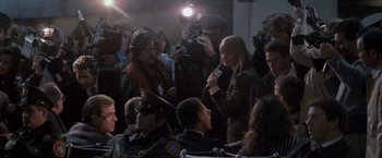 Movie still from “Die Hard 2” (1990), directed by Renny Harlin – A group of people gathered in a room with cameras and microphones; Medium shot, Over the shoulder angle