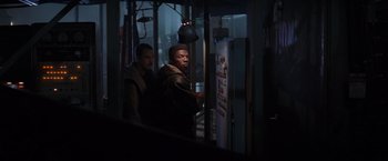 Movie still from “Die Hard 2” (1990), directed by Renny Harlin – Two men standing next to each other in a dark room; Medium shot, Over the shoulder angle