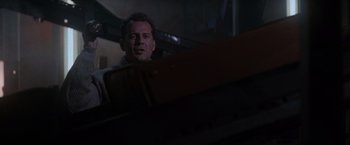 Movie still from “Die Hard 2” (1990), directed by Renny Harlin – A man standing in front of a piano in a dark room; Medium shot, Low angle