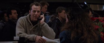 Movie still from “Die Hard 2” (1990), directed by Renny Harlin – A man talking on a cell phone while sitting at a table; Medium shot, Over the shoulder angle