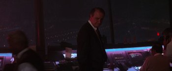 Movie still from “Die Hard 2” (1990), directed by Renny Harlin – A man in a suit standing in front of a computer desk; Medium shot, Low angle