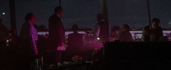 Movie still from “Die Hard 2” (1990), directed by Renny Harlin – A group of people standing in front of a large window at night; Extreme Wide shot, Over the shoulder angle