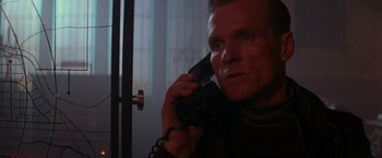 Movie still from “Die Hard 2” (1990), directed by Renny Harlin – A man talking on a phone while standing next to a door; Close Up shot, Low angle