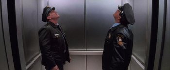 Movie still from “Die Hard 2” (1990), directed by Renny Harlin – Two men standing next to each other in front of an elevator; Medium shot, Low angle