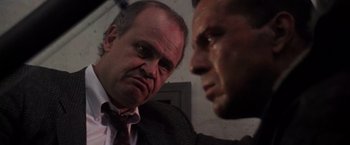 Movie still from “Die Hard 2” (1990), directed by Renny Harlin – Two men in business suits looking at each other; Close Up shot, Low angle