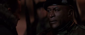 Movie still from “Die Hard 2” (1990), directed by Renny Harlin – A man wearing a black hat and a camouflage jacket; Close Up shot, Low angle