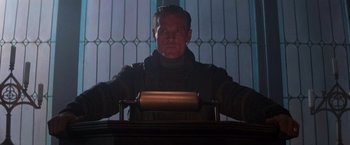 Movie still from “Die Hard 2” (1990), directed by Renny Harlin – A man standing at a table with a roll of paper; Medium shot, Low angle