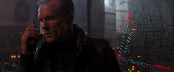 Movie still from “Die Hard 2” (1990), directed by Renny Harlin – A man standing in the dark with a city in the background; Close Up shot, Over the shoulder angle
