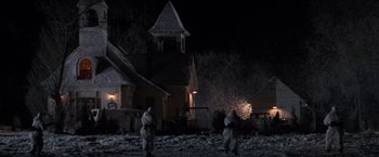 Movie still from “Die Hard 2” (1990), directed by Renny Harlin – A group of people walking in the snow near a house; Extreme Wide shot, Low angle