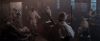 Movie still from “Die Hard 2” (1990), directed by Renny Harlin – A group of people in a room with a gun; Wide shot, High angle