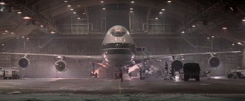 Movie still from “Die Hard 2” (1990), directed by Renny Harlin – An airplane is parked in a hangar at an airport; Extreme Wide shot, Low angle