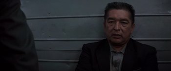 Movie still from “Die Hard with a Vengeance” (1995), directed by John McTiernan – A man in a suit and tie sitting in front of a wall; Close Up shot, Low angle