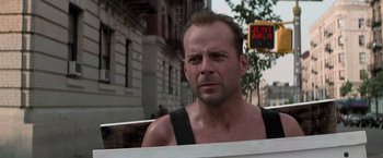 Movie still from “Die Hard with a Vengeance” (1995), directed by John McTiernan – A man in a tank top is standing in front of a building; Close Up shot, Low angle