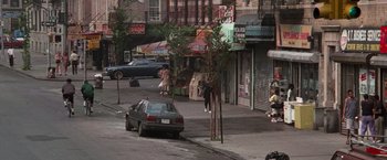 Movie still from “Die Hard with a Vengeance” (1995), directed by John McTiernan – A car parked on the side of the road near a building; Extreme Wide shot, High angle