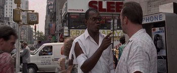 Movie still from “Die Hard with a Vengeance” (1995), directed by John McTiernan – A man in a white shirt is talking on a cell phone; Medium shot, Over the shoulder angle