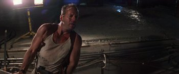 Movie still from “Die Hard with a Vengeance” (1995), directed by John McTiernan – A man in a white tank top is standing in the dark; Medium shot, Low angle