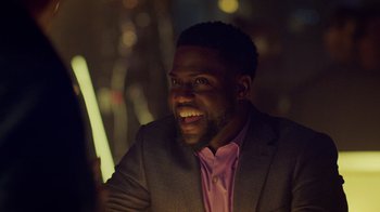 Movie still from “Die Hart” (2023), directed by Eric Appel – A person wearing a suit and smiling; Close Up shot, Over the shoulder angle