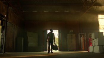 Movie still from “Die Hart” (2023), directed by Eric Appel – A man holding a bag while standing in front of an open door; Extreme Wide shot, Low angle