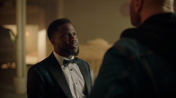Movie still from “Die Hart” (2023), directed by Eric Appel – A man in a tuxedo is talking to another man in a suit; Medium shot, Over the shoulder angle