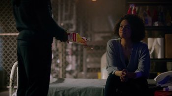 Movie still from “Die Hart” (2023), directed by Eric Appel – A woman sitting on a bed and a man handing a package to another person; Medium shot, Over the shoulder angle