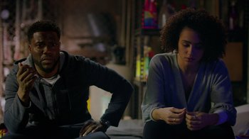 Movie still from “Die Hart” (2023), directed by Eric Appel – A man and a woman sitting next to each other on a couch; Medium shot, Over the shoulder angle