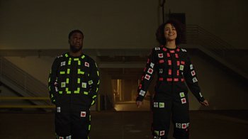 Movie still from “Die Hart” (2023), directed by Eric Appel – A man and a woman in black and yellow clothes; Medium shot, Over the shoulder angle