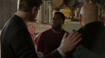 Movie still from “Die Hart” (2023), directed by Eric Appel – A man is talking to two other men in a warehouse; Medium shot, Over the shoulder angle