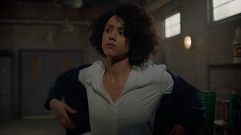 Movie still from “Die Hart” (2023), directed by Eric Appel – A woman with curly black hair standing in a dark room; Medium shot, Over the shoulder angle